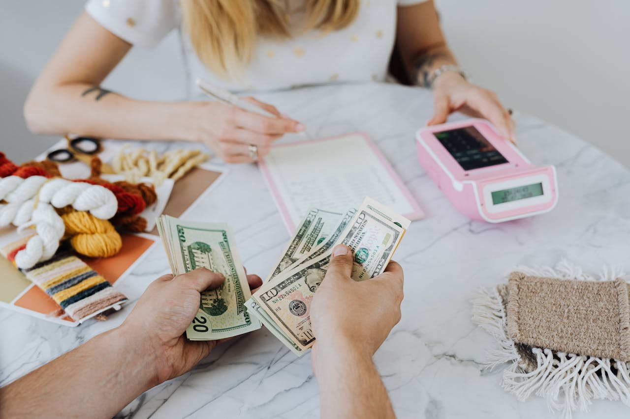 about-img Two people handling cash and budgeting with a calculator and notebook at a table.